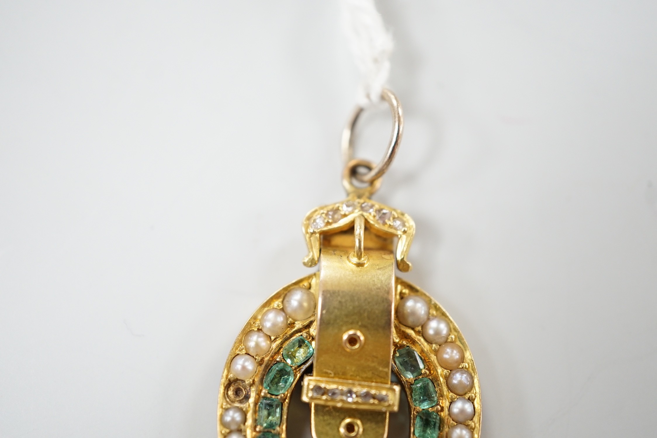An early 20th century yellow metal, emerald, rose cut diamond and split pearl set horseshoe and buckle pendant, 33mm, gross weight 6 grams.